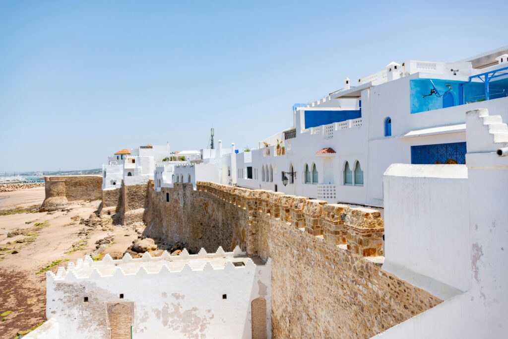 A view of a whitewashed medina with an ancient seaside fortress under a clear blue sky in Morocco.