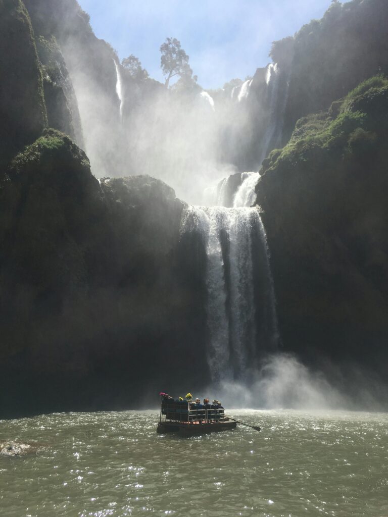 Stunning view of Ouzoud Falls in Morocco with tourists on a raft below the cascading waterfalls.